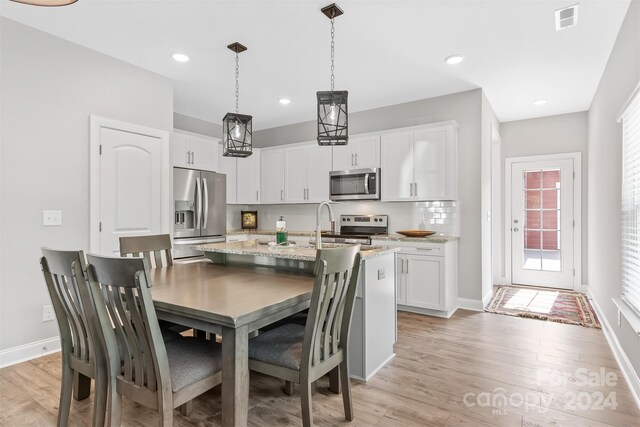 kitchen with light stone counters, appliances with stainless steel finishes, white cabinets, and light hardwood / wood-style floors