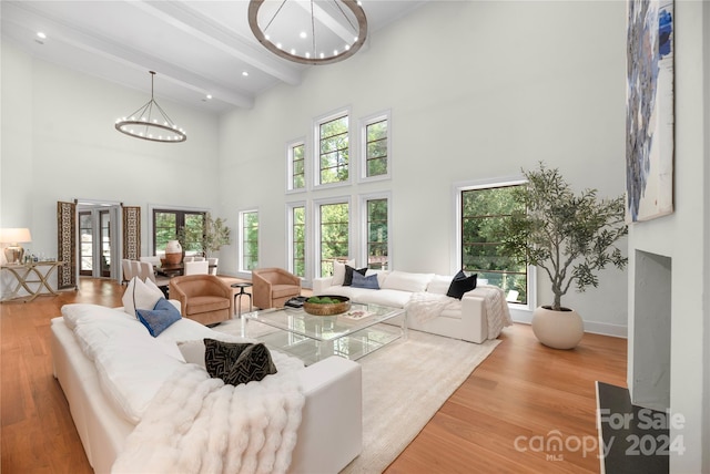 living room featuring an inviting chandelier, beam ceiling, a towering ceiling, and light hardwood / wood-style floors