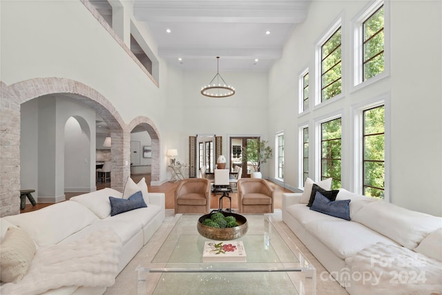 interior space with light wood-type flooring, a notable chandelier, beamed ceiling, and a high ceiling