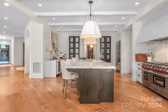 kitchen featuring light hardwood / wood-style flooring, sink, an island with sink, range with two ovens, and a kitchen breakfast bar