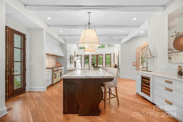 kitchen featuring wine cooler, beamed ceiling, french doors, light stone counters, and light wood-type flooring