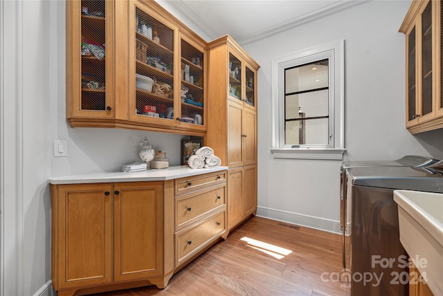 laundry room featuring crown molding, cabinets, washer and clothes dryer, and light hardwood / wood-style floors