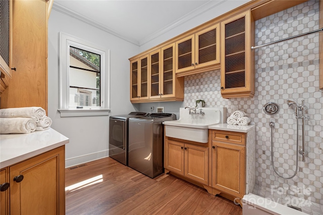 laundry area featuring cabinets, ornamental molding, separate washer and dryer, wood-type flooring, and sink