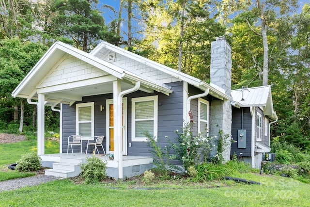 view of front of home featuring a front yard, a porch, a chimney, crawl space, and metal roof