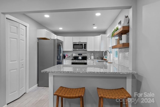 kitchen featuring open shelves, a sink, appliances with stainless steel finishes, a peninsula, and white cabinets