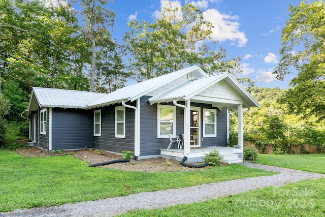 view of front of home featuring metal roof, covered porch, and a front yard