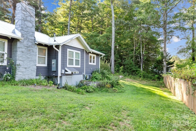 view of home's exterior featuring a lawn, fence, metal roof, central AC unit, and a chimney