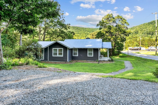 view of front facade with driveway, metal roof, and a front lawn