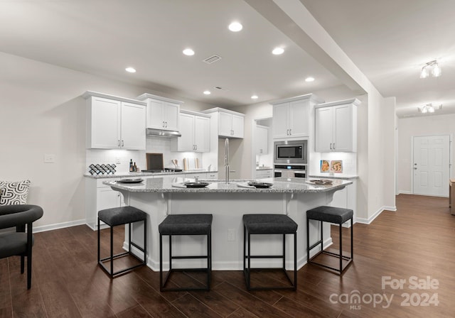 kitchen with under cabinet range hood, white cabinetry, appliances with stainless steel finishes, and dark wood finished floors