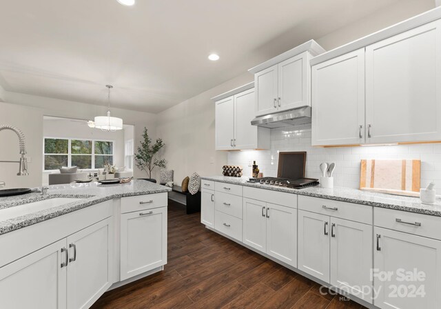 kitchen with dark wood-style flooring, stainless steel gas cooktop, decorative backsplash, white cabinetry, and under cabinet range hood