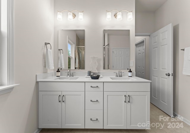 bathroom with double vanity, a shower, a sink, and baseboards