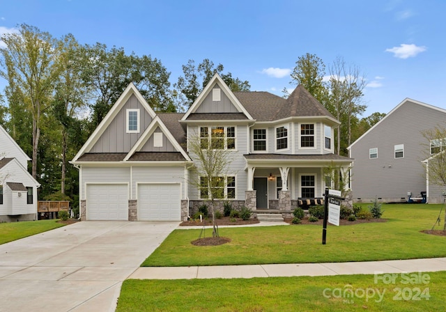 view of front of home with covered porch, concrete driveway, stone siding, board and batten siding, and a front yard