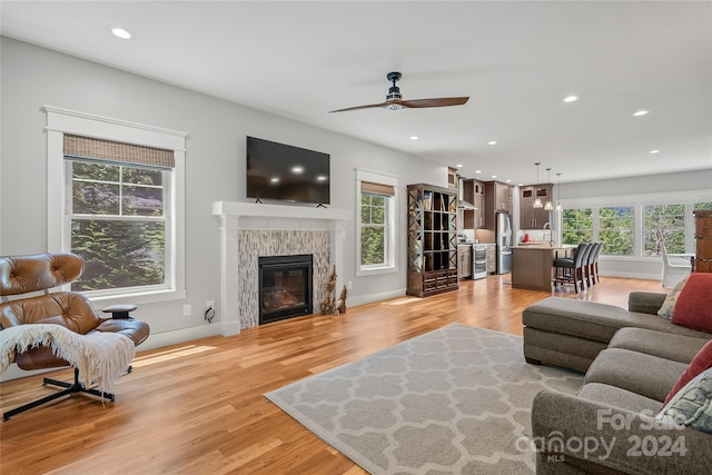 living room with light wood-type flooring, a fireplace, a healthy amount of sunlight, and ceiling fan