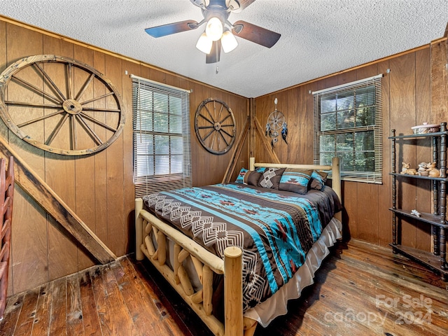 bedroom with a textured ceiling, a ceiling fan, ornamental molding, hardwood / wood-style floors, and wood walls
