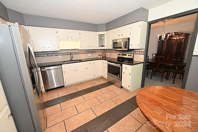 kitchen with white cabinets, dark countertops, an inviting chandelier, stainless steel appliances, and a sink