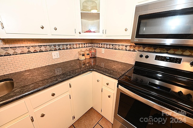 kitchen featuring tasteful backsplash, glass insert cabinets, dark stone countertops, stainless steel appliances, and white cabinetry