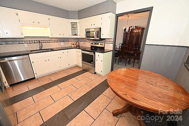 kitchen featuring white cabinets, dark countertops, stainless steel appliances, a chandelier, and a sink