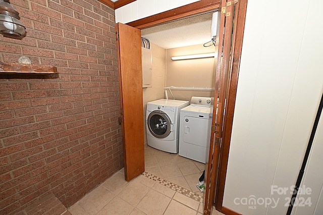 washroom with light tile patterned floors, a textured ceiling, brick wall, laundry area, and washing machine and clothes dryer