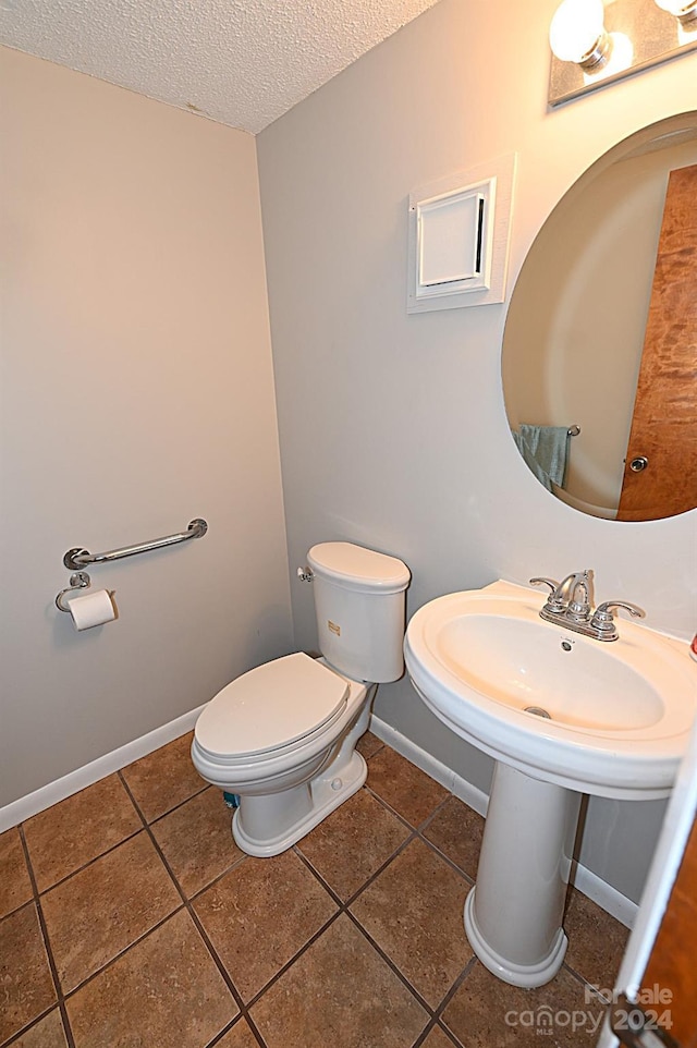 bathroom with a textured ceiling, baseboards, toilet, and tile patterned floors