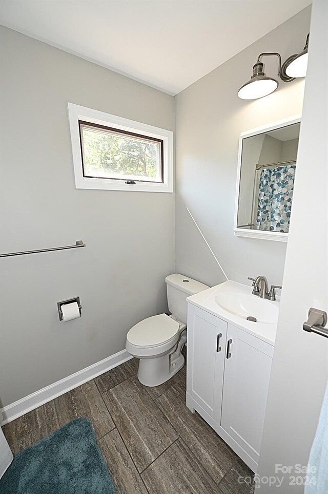 bathroom with toilet, wood finished floors, vanity, and baseboards