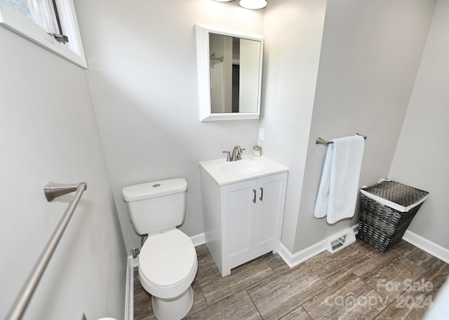 bathroom with toilet, wood finish floors, visible vents, vanity, and baseboards