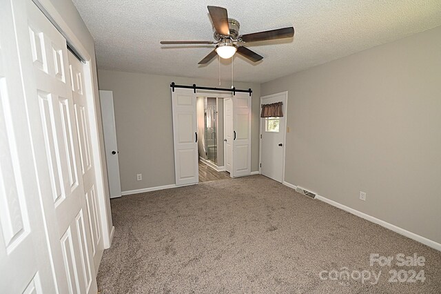 unfurnished bedroom featuring a barn door, baseboards, visible vents, a textured ceiling, and carpet flooring