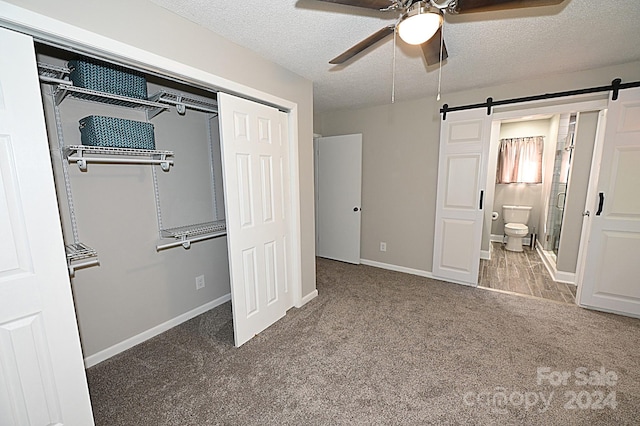 unfurnished bedroom featuring carpet, a closet, a barn door, a textured ceiling, and baseboards