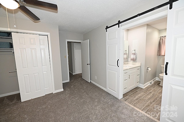 unfurnished bedroom with a textured ceiling, a barn door, baseboards, a closet, and ensuite bath