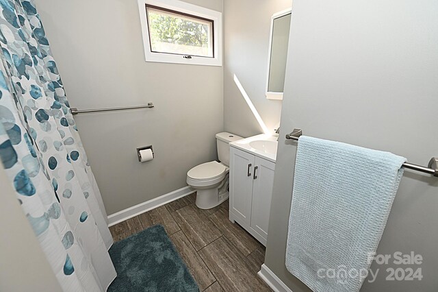 bathroom with a shower with shower curtain, toilet, vanity, wood finished floors, and baseboards