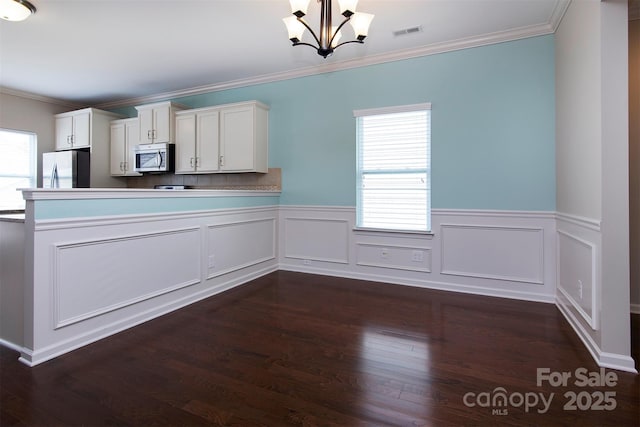 kitchen with pendant lighting, appliances with stainless steel finishes, ornamental molding, white cabinets, and a chandelier