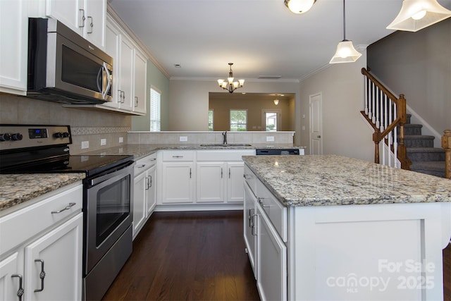 kitchen with hanging light fixtures, stainless steel appliances, white cabinets, and a kitchen island