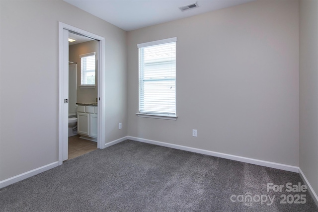 unfurnished bedroom featuring ensuite bathroom and dark carpet