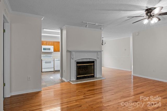 unfurnished living room with light hardwood / wood-style floors, a tiled fireplace, track lighting, ceiling fan, and crown molding