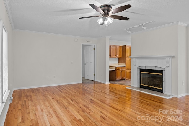 unfurnished living room featuring light wood-type flooring, a textured ceiling, track lighting, a tile fireplace, and ceiling fan