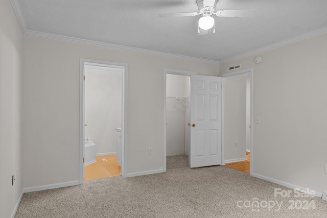 unfurnished bedroom featuring ceiling fan, a walk in closet, ensuite bathroom, carpet floors, and crown molding