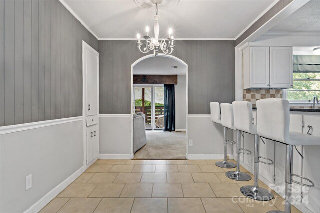 unfurnished dining area with plenty of natural light, ornamental molding, light tile patterned floors, and an inviting chandelier