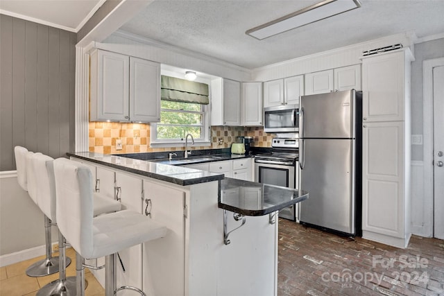 kitchen with dark countertops, appliances with stainless steel finishes, ornamental molding, a peninsula, and a sink