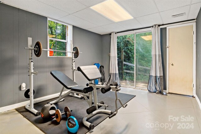 exercise area with a drop ceiling, tile patterned flooring, and wooden walls