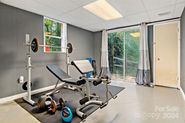 exercise room with a paneled ceiling, baseboards, floor to ceiling windows, and visible vents