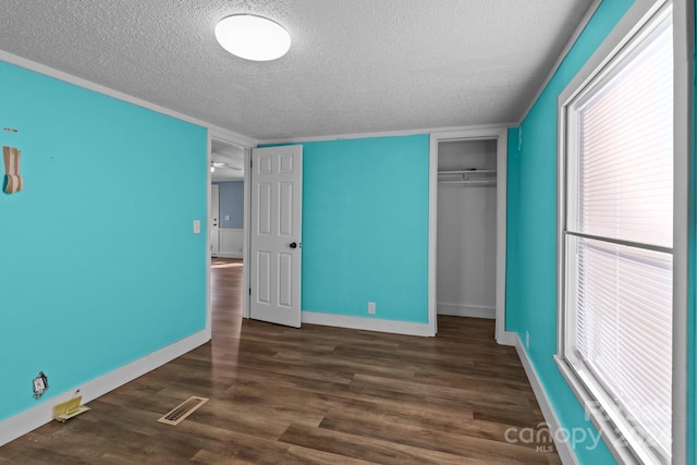 unfurnished bedroom featuring a textured ceiling, a closet, multiple windows, and dark hardwood / wood-style flooring