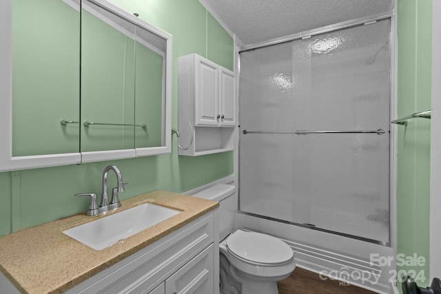 full bathroom featuring shower / bath combination with glass door, vanity, wood-type flooring, a textured ceiling, and toilet