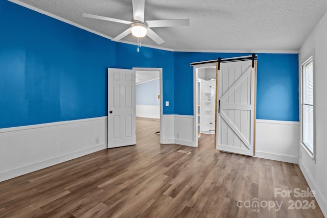 unfurnished bedroom with a textured ceiling, ceiling fan, wood-type flooring, and a barn door