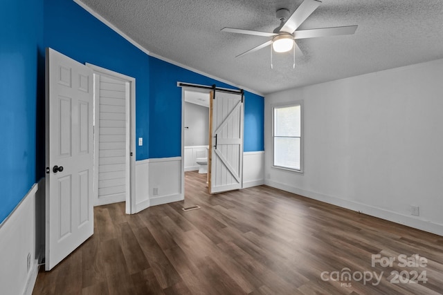 unfurnished bedroom featuring ceiling fan, a textured ceiling, dark hardwood / wood-style floors, and a barn door