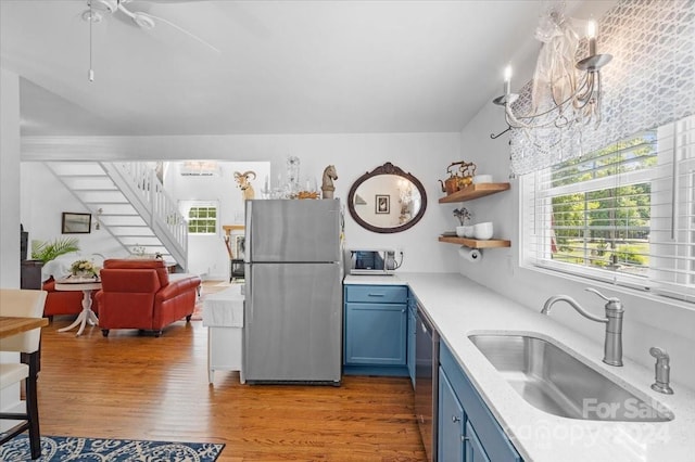 kitchen with blue cabinets, sink, appliances with stainless steel finishes, an inviting chandelier, and light wood-type flooring