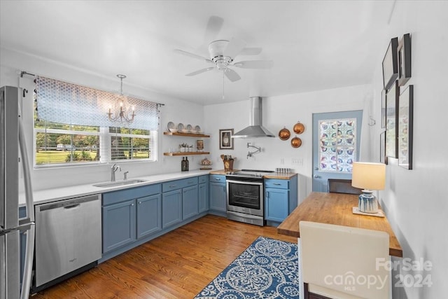 kitchen with hanging light fixtures, sink, wall chimney range hood, stainless steel appliances, and light hardwood / wood-style floors