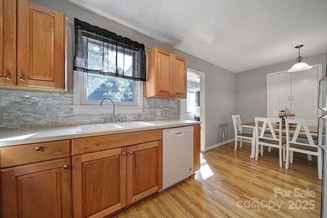 kitchen with pendant lighting, white dishwasher, sink, decorative backsplash, and light wood-type flooring