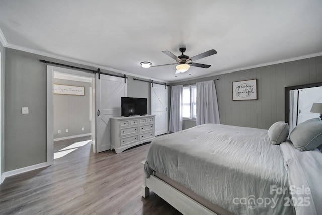 bedroom featuring light hardwood / wood-style floors, ceiling fan, a barn door, and ornamental molding