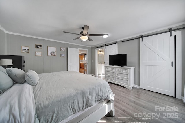 bedroom featuring ceiling fan, a barn door, ornamental molding, and ensuite bath