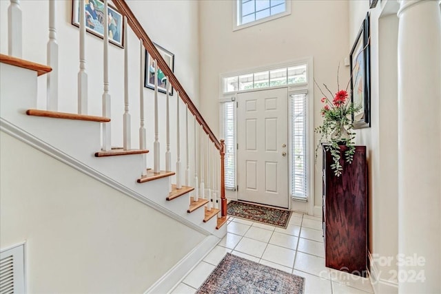 entrance foyer featuring baseboards, visible vents, tile patterned flooring, stairs, and a towering ceiling