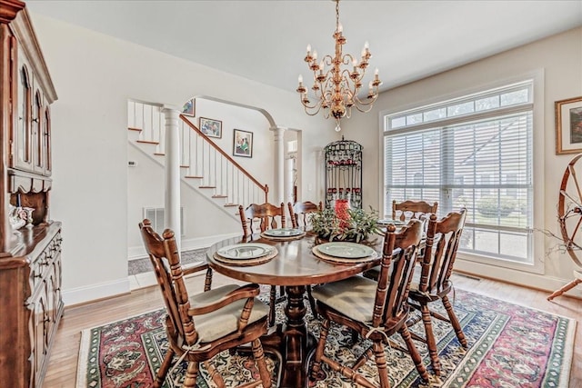 dining space with baseboards, light wood-type flooring, stairs, decorative columns, and arched walkways